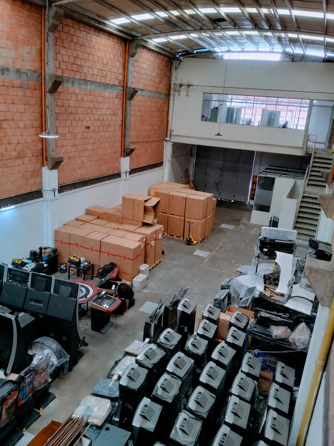 Vista general de la bodega de Slot Tech desde el altillo, con gabinetes de tragamonedas, monitores embalados y mercancía en estibas